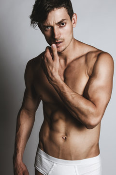Portrair of a male model with perfect body in white underwear posing over grey background. Close-up. Studio shot.