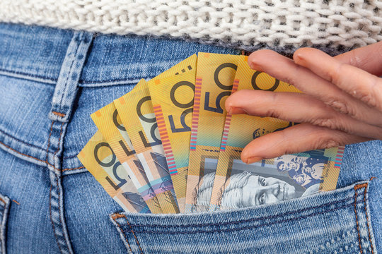Female hand reaching for 50 Australian dollar bills in her jeans back pocket
