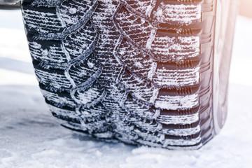 The car tire in the snow close up. Car tracks on the snow. Traces of the car in the snow. Winter tires. Tyres covered with snow at winter road. Soft lightning