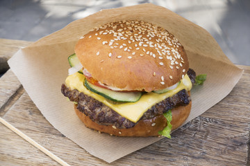Fresh juicy tasty burger with beef on wooden table in craft paper