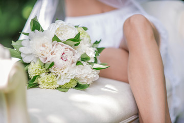 Obraz na płótnie Canvas Beautiful white bouquet of peonies lies by bride knees on a couch