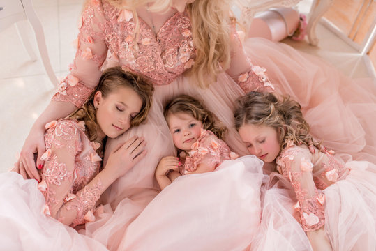 Three girls in pink dresses sleep on mom's knees