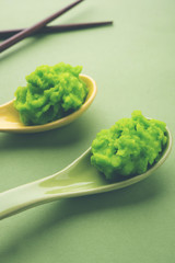 Green wasabi sauce or paste in bowl, with chopsticks or spoon over plain colourful background. selective focus