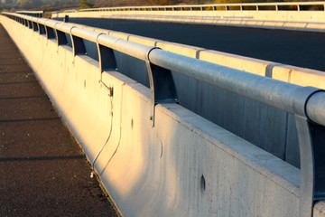 Concrete road bridge barrier with strong metal safety guard rails mounted on top at sunset