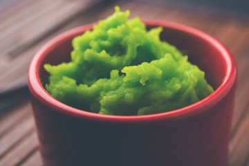 Green wasabi sauce or paste in bowl, with chopsticks or spoon over plain colourful background. selective focus
