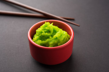 Green wasabi sauce or paste in bowl, with chopsticks or spoon over plain colourful background. selective focus