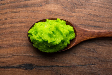 Green wasabi sauce or paste in bowl, with chopsticks or spoon over plain colourful background. selective focus