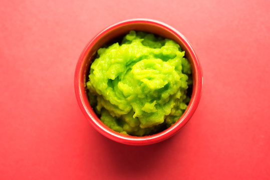 Green wasabi sauce or paste in bowl, with chopsticks or spoon over plain colourful background. selective focus