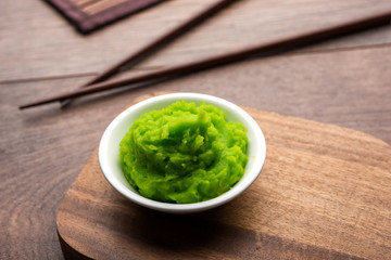 Green wasabi sauce or paste in bowl, with chopsticks or spoon over plain colourful background. selective focus