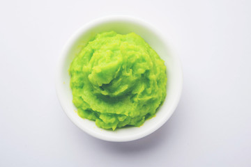 Green wasabi sauce or paste in bowl, with chopsticks or spoon over plain colourful background. selective focus