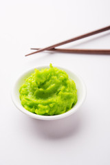 Green wasabi sauce or paste in bowl, with chopsticks or spoon over plain colourful background. selective focus