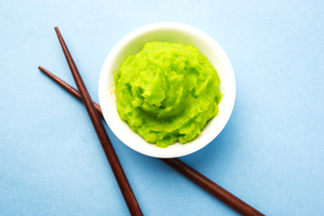 Green wasabi sauce or paste in bowl, with chopsticks or spoon over plain colourful background. selective focus
