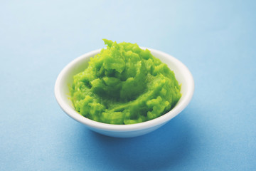 Green wasabi sauce or paste in bowl, with chopsticks or spoon over plain colourful background. selective focus