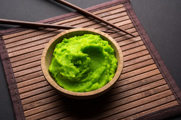 Green wasabi sauce or paste in bowl, with chopsticks or spoon over plain colourful background. selective focus