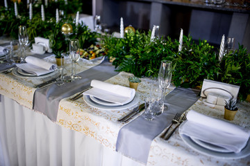 White dinner table decorated with greenery and white candles stands in the hall prepared for wedding