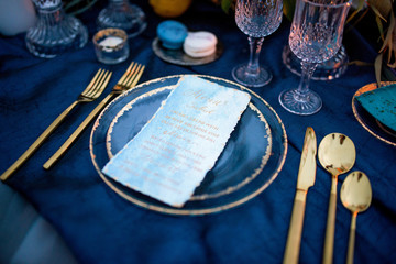 Menu card lies on a blue plate surrounded with golden dinner set