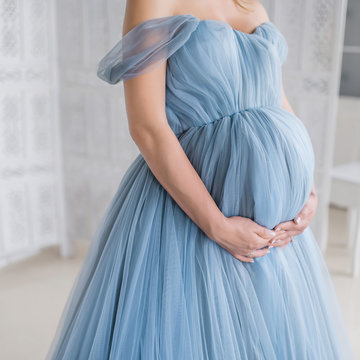 Pregnant woman in pink dress holds hands on her belly