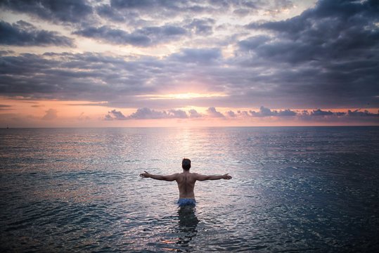 Fototapeta Man stands in the sea water facing sunset