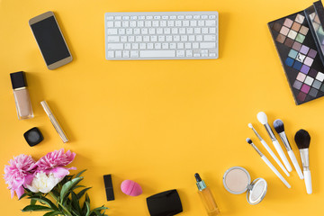 View from above of fashion blogger workspace with white keyboard, female accessory, cosmetics products on yellow background. flat lay, beauty business concept