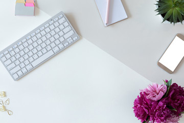 Top view of white office table desk or woman workspace with computer keyboard, diary, pink bouquet of peony flowers background. Flat lay