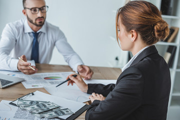 financiers pointing on documents at table in office