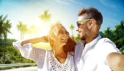 Two young lovers on summer trip and background with palms and sun light. 