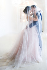 Groom and bride in pink dress stand kissing under the veil