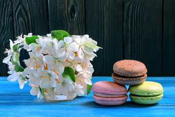 Multicolored macaroons and cup decorated with white flowers of apple trees on a blue wooden background.