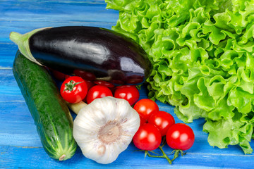 Different raw vegetables lies in a heap on a blue wooden table.