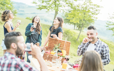 Happy millennials friends drinking wine and eating appetizer snack at picnic in nature