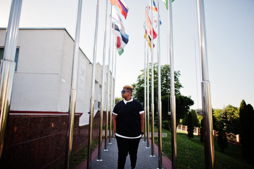 Stylish arabian muslim boy with originally hair posed on streets, against flags of different countries.