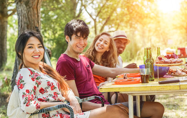 Multicultural happy friends eating and drinking beers at barbecue dinner at sunset