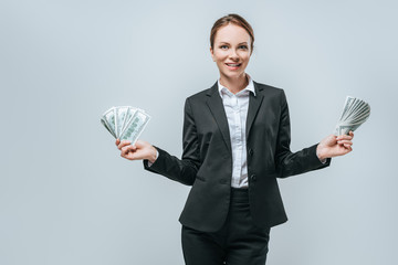 attractive financier holding dollars in hands and looking at camera isolated on grey