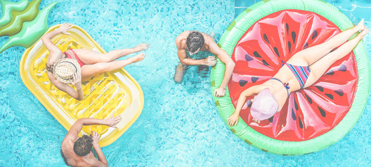 Happy millennials friends having fun floating in swimming pool - Young people enjoying summer...