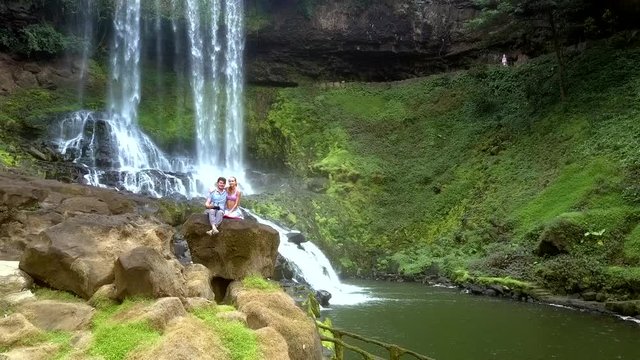 guy girl sit on rock by waterfall in park
