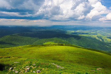 Fototapeta na wymiar grassy hillside view from above. beautiful summer landscape of mountainous area. huge clouds a bright day. rain on the far distant mountain