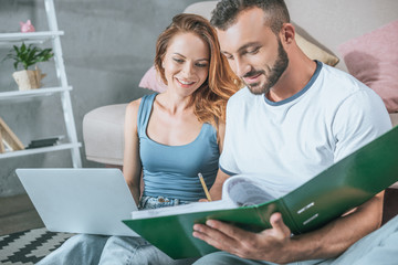 happy couple planning family budget in living room with laptop and folder