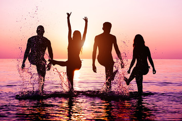 Happy friends splashing water on tropical beach at sunset