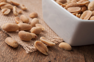 closeup of salted peanuts in a porcelain bowl on wooden background
