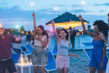 Happy friends having fun beach party outdoor with fireworks
