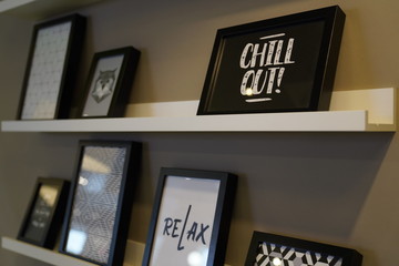 Frames on a shelf on a grey wall with writings of «Chill out» and «Relax»