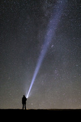 Silhouette of a tourist with a flashlight, observing beautiful, wide blue night sky with stars and galaxies