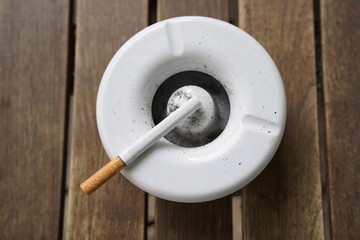 White ashtray with a non lit cigarette on it standing on a brown wooden table