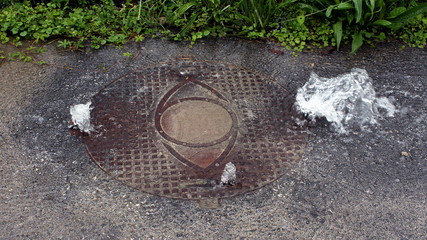 Heavy duty bolted sewer manhole cover heavily leaking water from enormous flood pressure in the...