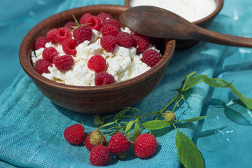 raspberry branch with berries cottage cheese sour cream in earthenware on cloth blue background close-up