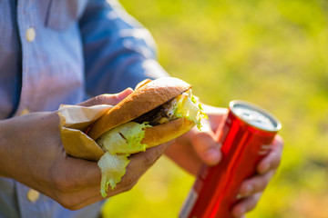 man in a shirt holds a burger and a sweet fizzy drink