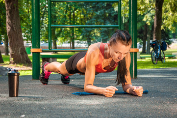 girl athlete doing plank exercise on elbows in the park on the playground.