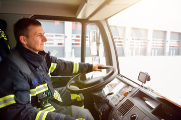 Obraz premium smiling fireman at the wheel of a fire truck drives to work
