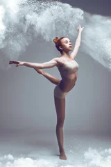 Zelfklevend Fotobehang Dansen in meelconcept. Roodharige sportieve performer vrouw in stof/mist. Meisje met witte top en korte broek die danselement maakt in bloemwolk op geïsoleerde achtergrond © Monstar Studio