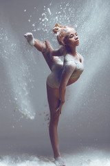 Dancing in flour concept. Redhead sporty performer woman in dust / fog. Girl wearing white top and shorts making dance element in flour cloud on isolated background